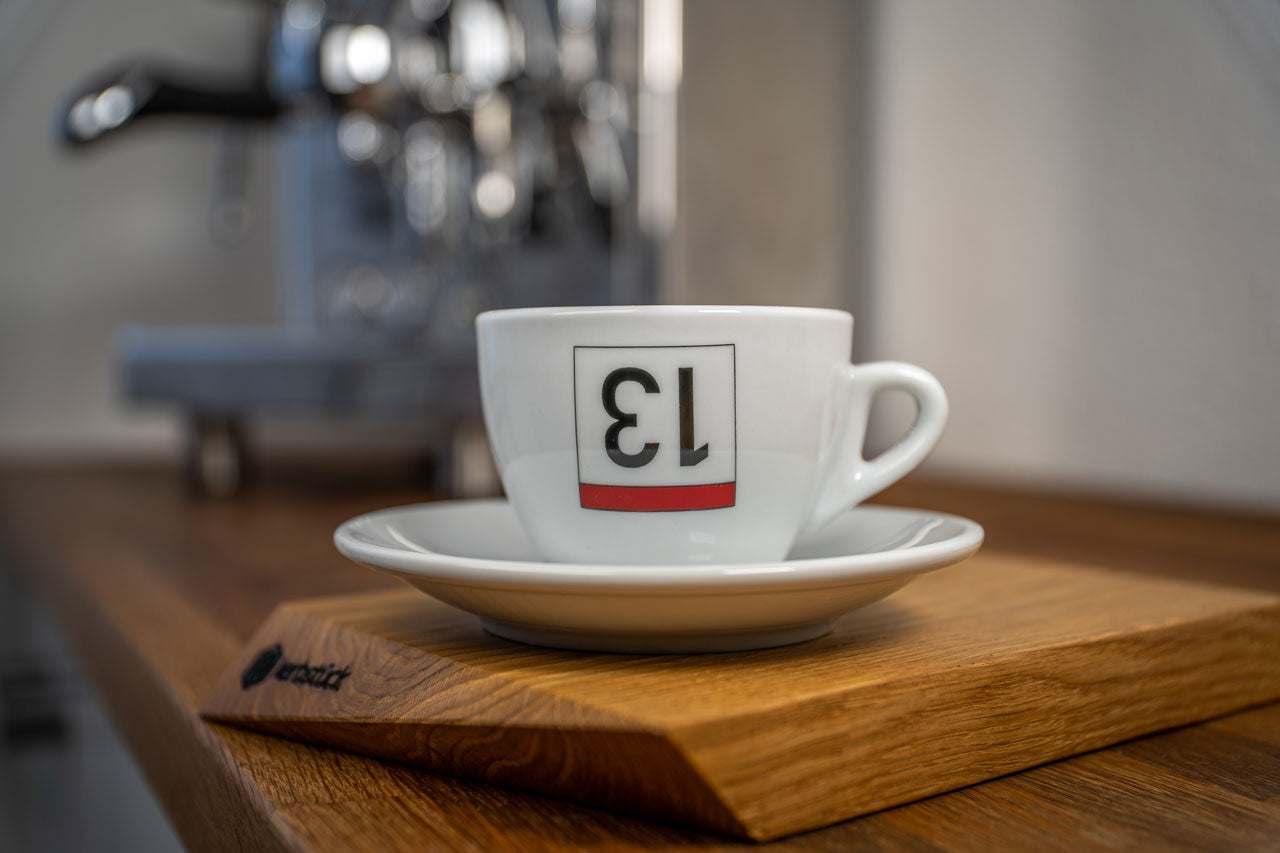 Eine weiße Cappuccino-Tasse bedruckt mit einer umgedrehten 13 als stilisierte Rückennummer.