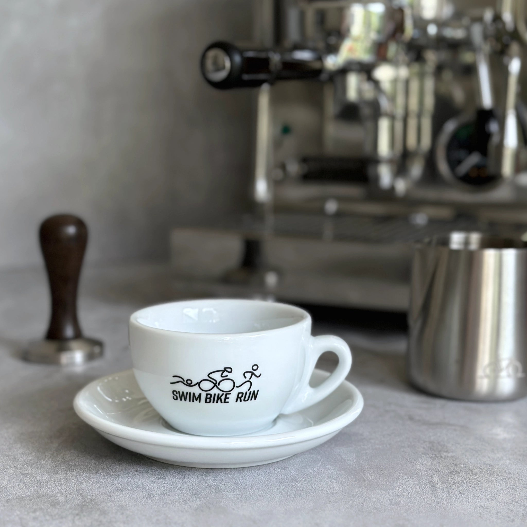 Cappuccino Grande Tasse mit Triathlon-Motiv vor Siebträgermaschine