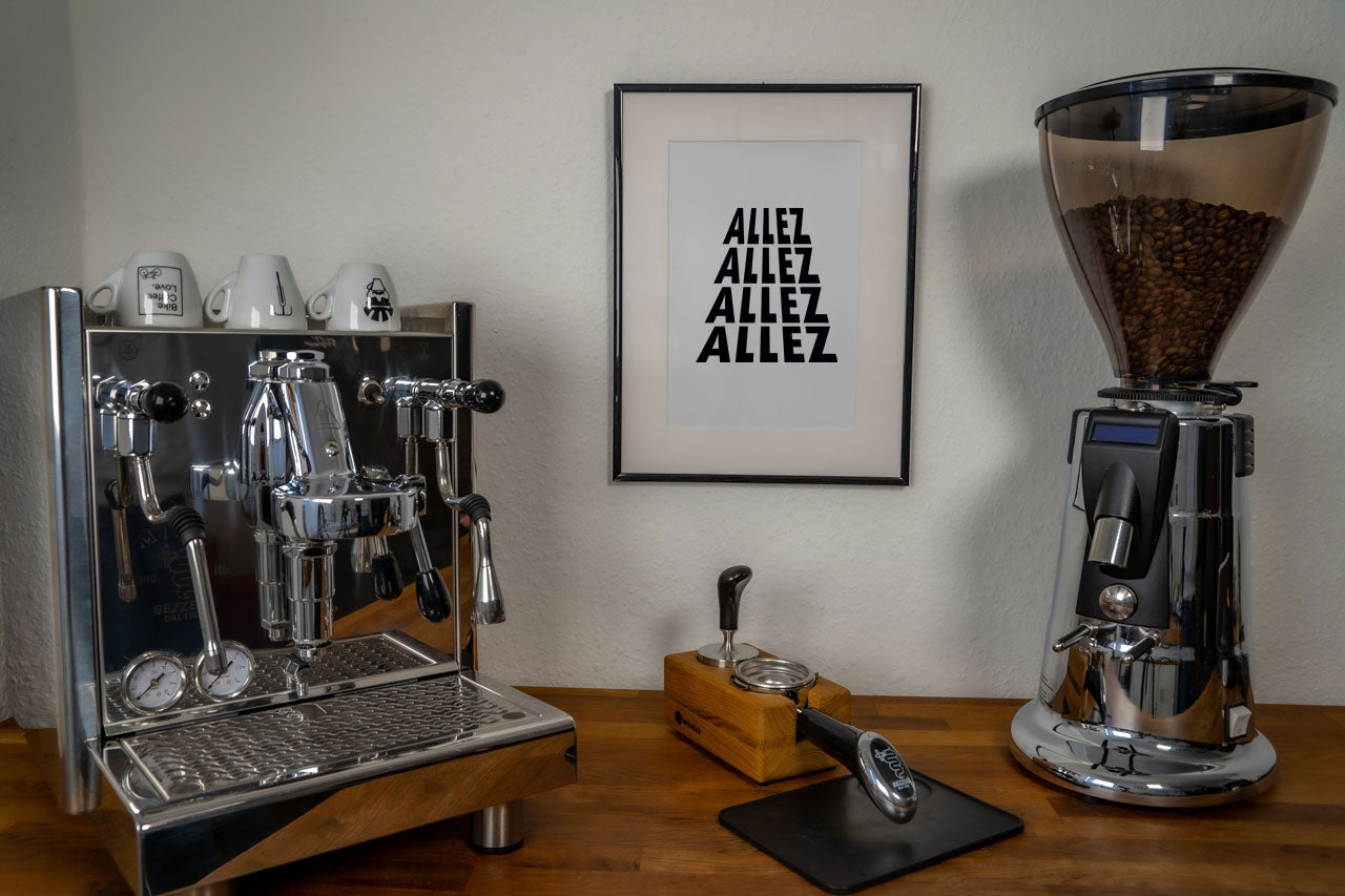 Das Poster "Allez" hängt im Bilderrahmen an der Wand zwischen einer Kaffeemaschine und einer Kaffeemühle.