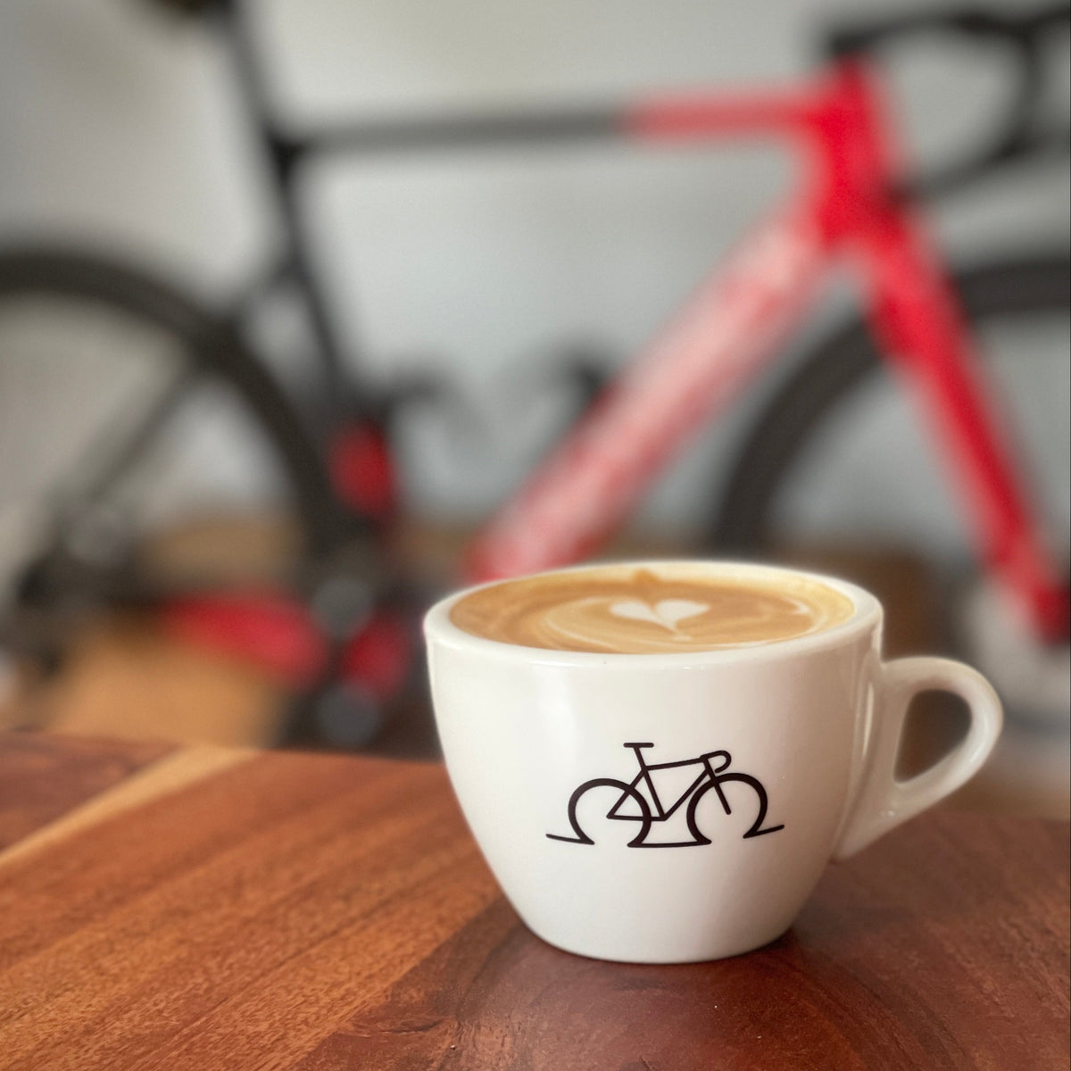 CYCLEBEAN Espressotasse mit Fahrrad-Print und Kaffee vor unscharfem Rennrad