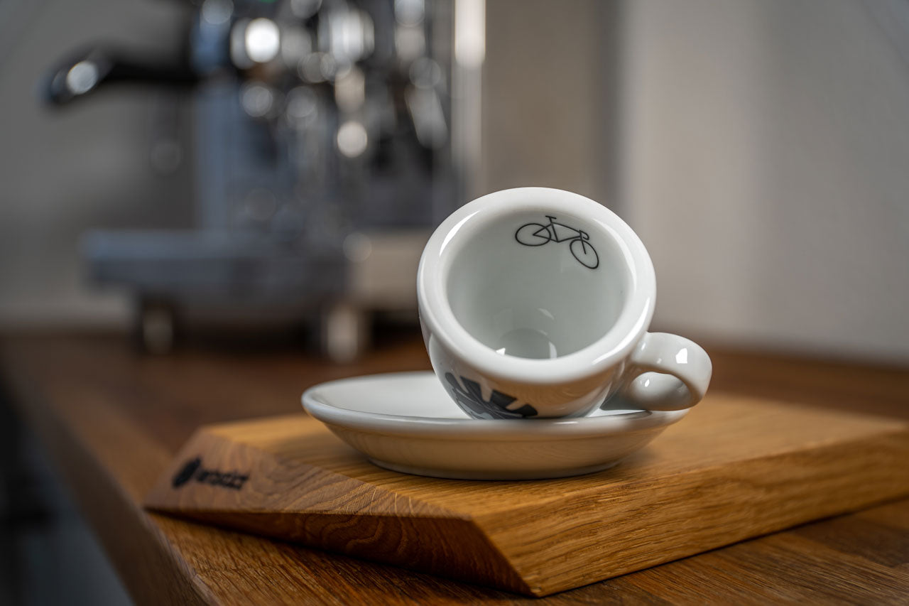 Eine Espresso-Tasse liegt auf der Seite, auf dem inneren Tassenrand ist ein Rennrad abgedruckt.
