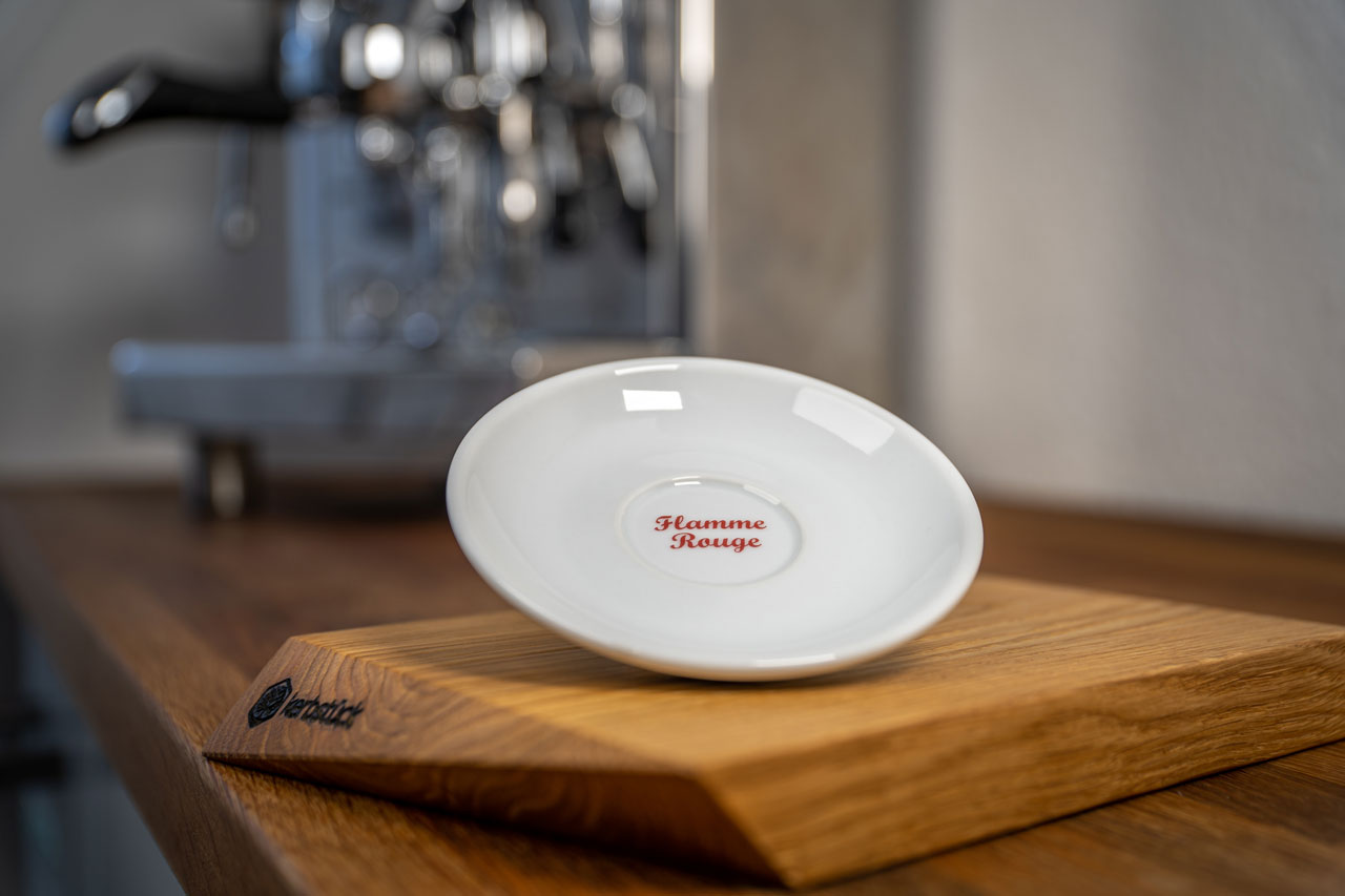 Eine weiße Untertasse mit dem verschnörkelten Schriftzug "Flamme rouge".